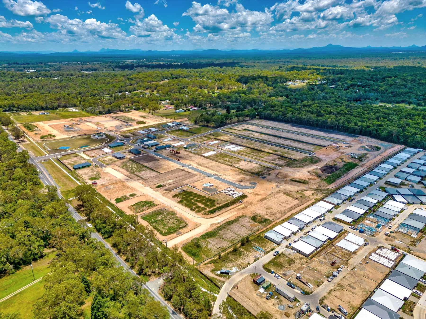 Aerial of the Sungold Road residential subdivision mid-delivery with freshly cut lots and earthworks in the foreground, partially built homes at right, surrounding bushland and distant mountains