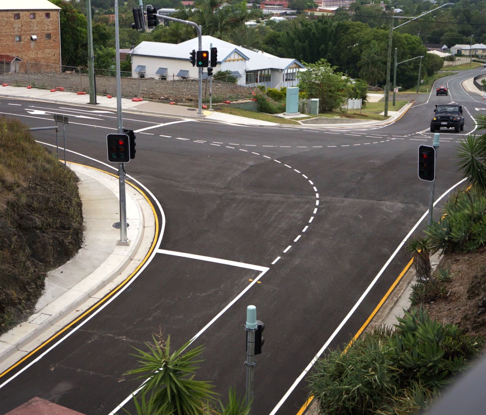 Newly completed Station Road intersection upgrade showing fresh asphalt, crisp white line marking, yellow kerbs, new traffic signals, and a vehicle approaching from the upper right